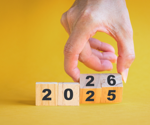 Hand adjusting wooden blocks displaying the numbers 2025 and 2026, against a yellow background, symbolizing the transition into the new local search reality for 2026.
